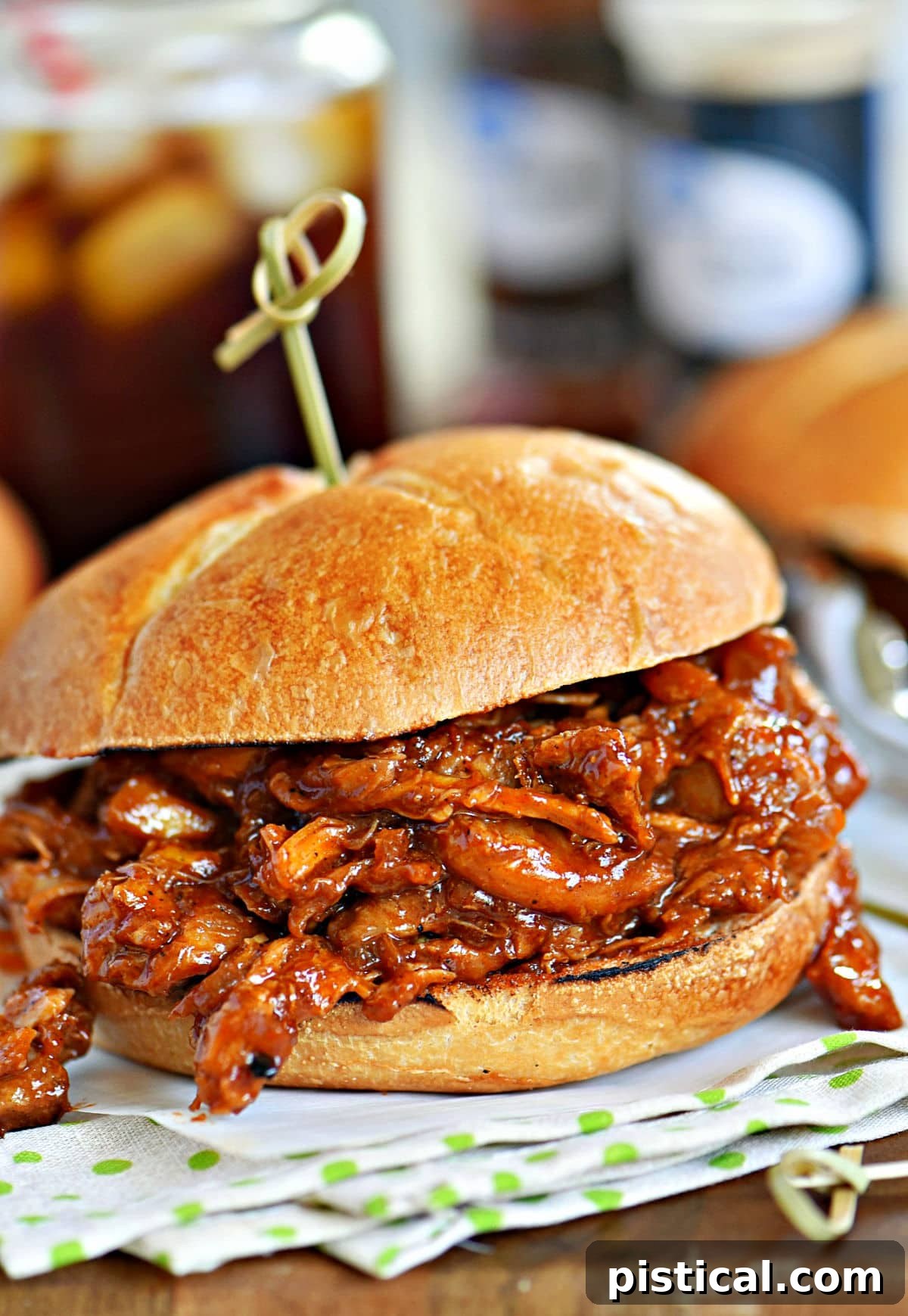 A delicious BBQ pulled chicken sandwich, artfully placed on a green and white napkin, showcasing the rich pulled chicken and toasted bun.