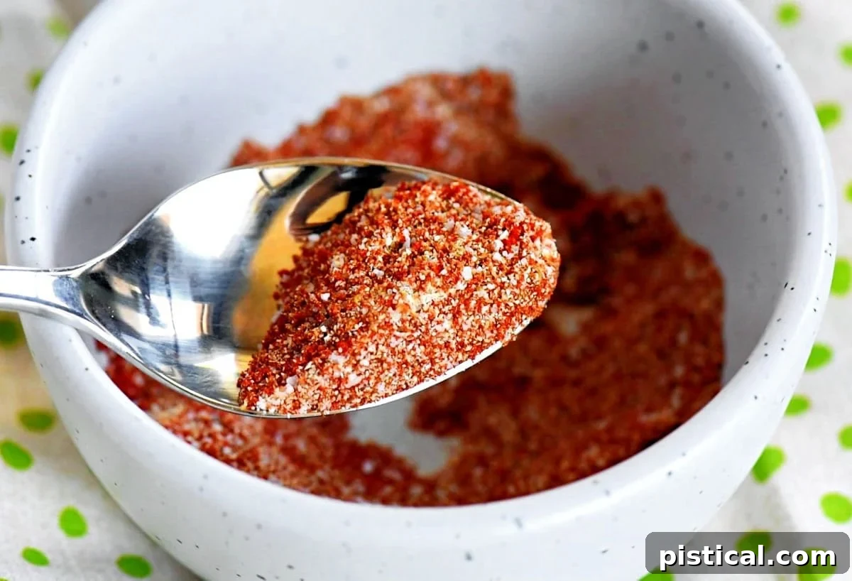 A small bowl containing a vibrant seasoning blend, ready to be rubbed onto chicken thighs. A spoon holds a portion of the seasoning above the bowl, highlighting its texture and color.