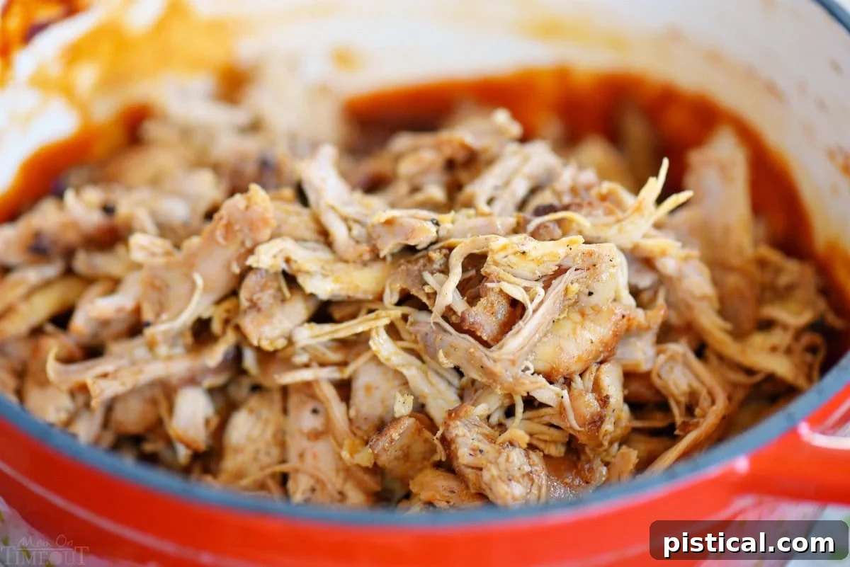 Shredded pulled chicken being stirred into a pot of simmering root beer BBQ sauce, ready to be coated in flavor.