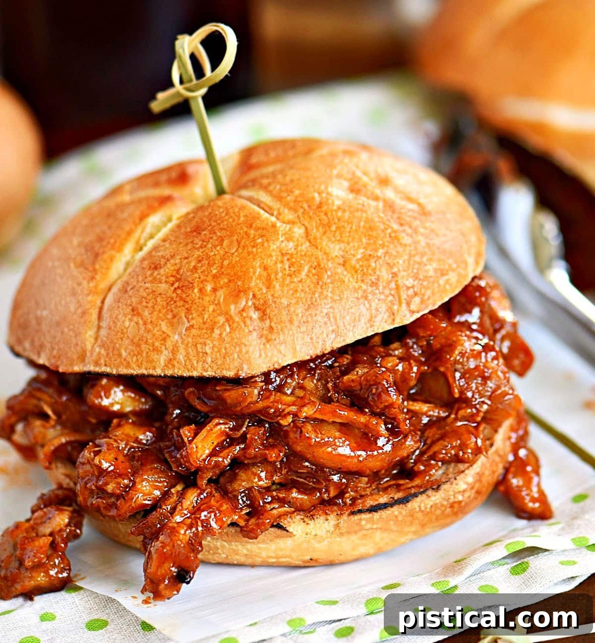 A perfectly assembled BBQ pulled chicken sandwich on a toasted bun, secured with a decorative toothpick, ready to be enjoyed.