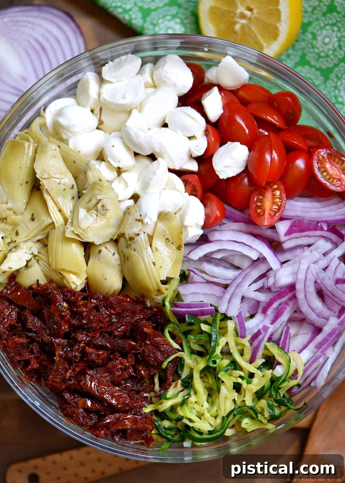 Key ingredients for an easy and delicious Zucchini Pasta Salad recipe, featuring a blend of fresh produce and convenient pantry staples for a quick summer meal. Assortment of fresh and jarred ingredients laid out for Zucchini Pasta Salad preparation, including pasta, zucchini spirals, mozzarella, sun-dried tomatoes, and artichokes.