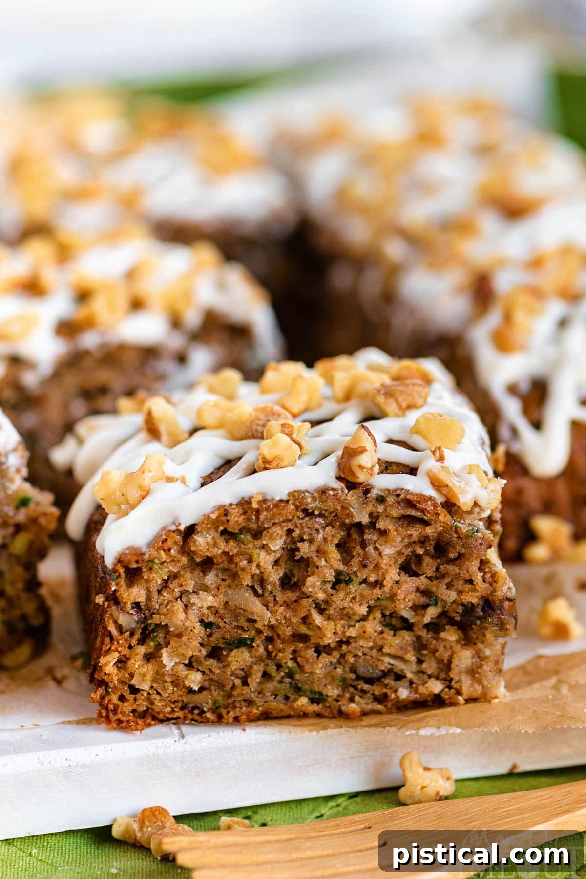 A close-up view of a single slice of zucchini spice cake, elegantly frosted with cream cheese icing and topped with chopped walnuts, sitting on a white plate with a fork poised to cut into it.