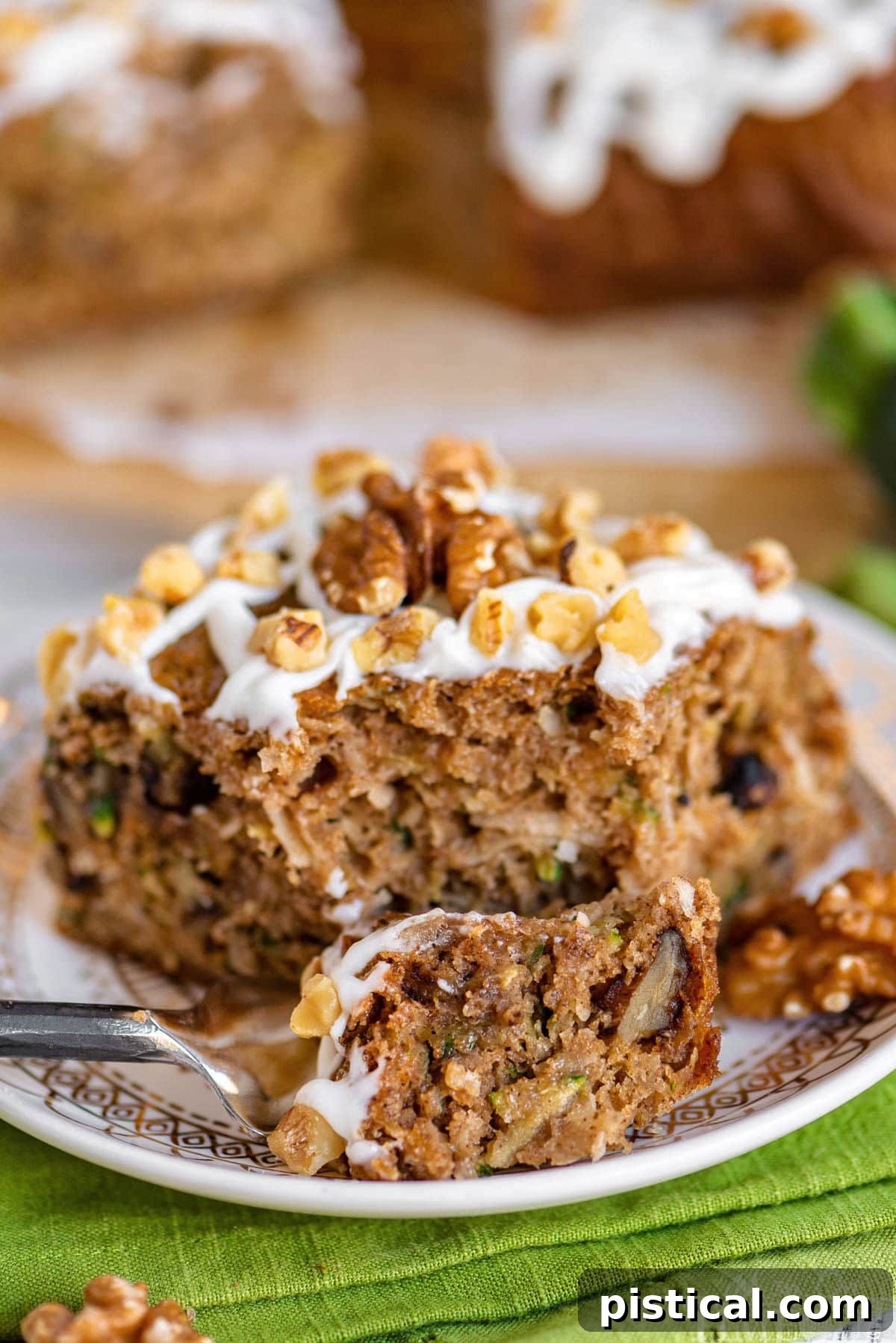 A beautiful piece of zucchini spice cake on a white round plate, with a fork gently cutting into one corner, highlighting the moist texture and creamy frosting.