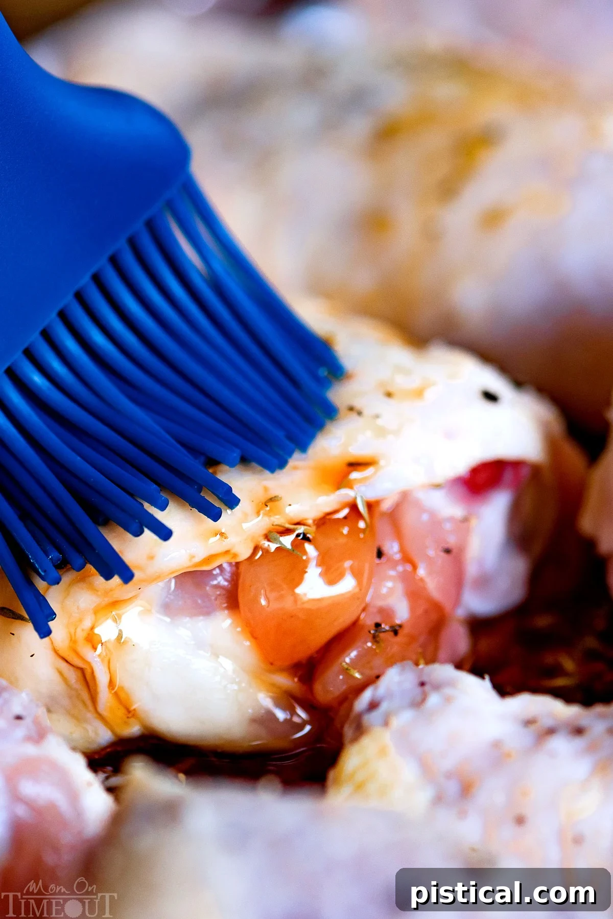 A hand brushing the delicious honey balsamic glaze onto chicken pieces on a baking sheet before roasting.