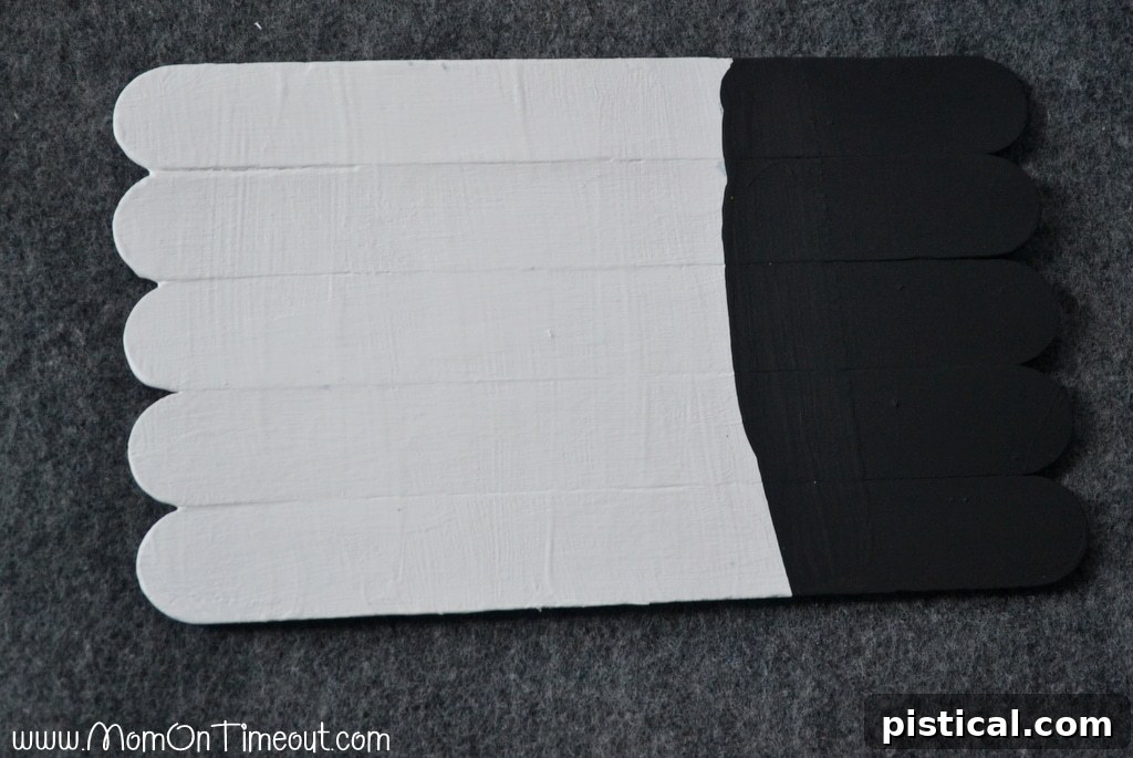 Step-by-step guide: Painting the craft stick snowman with black for the hat and white for the face.