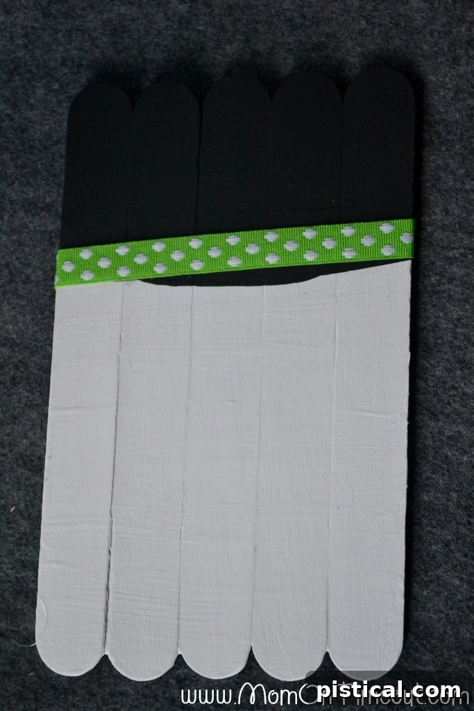 Step-by-step guide: Attaching a decorative ribbon to the painted black hat section of the craft stick snowman.