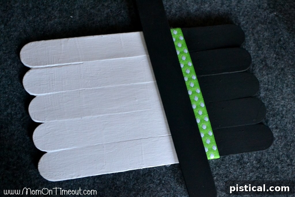 Step-by-step guide: Gluing the black painted craft stick to form the hat brim of the snowman ornament.