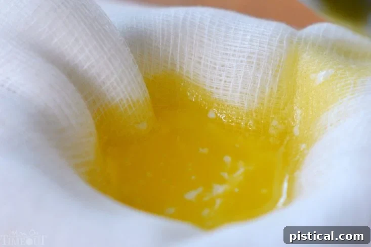 Straining melted butter through multiple layers of cheesecloth into a glass jar.