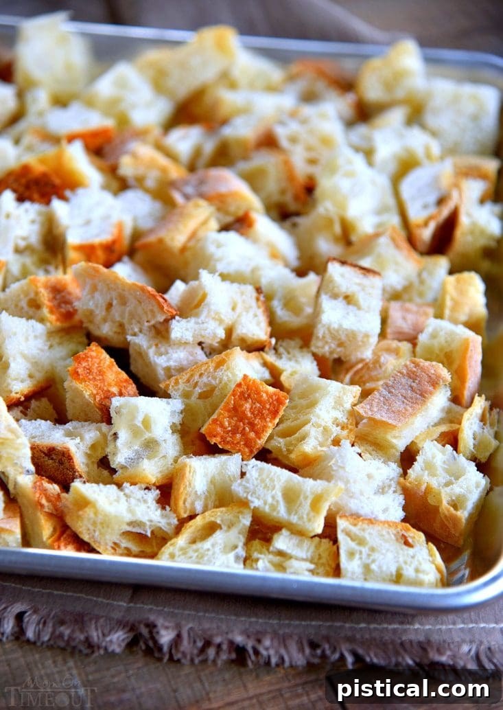 Cubed bread spread on a baking sheet, being toasted in the oven to dry out for stuffing.