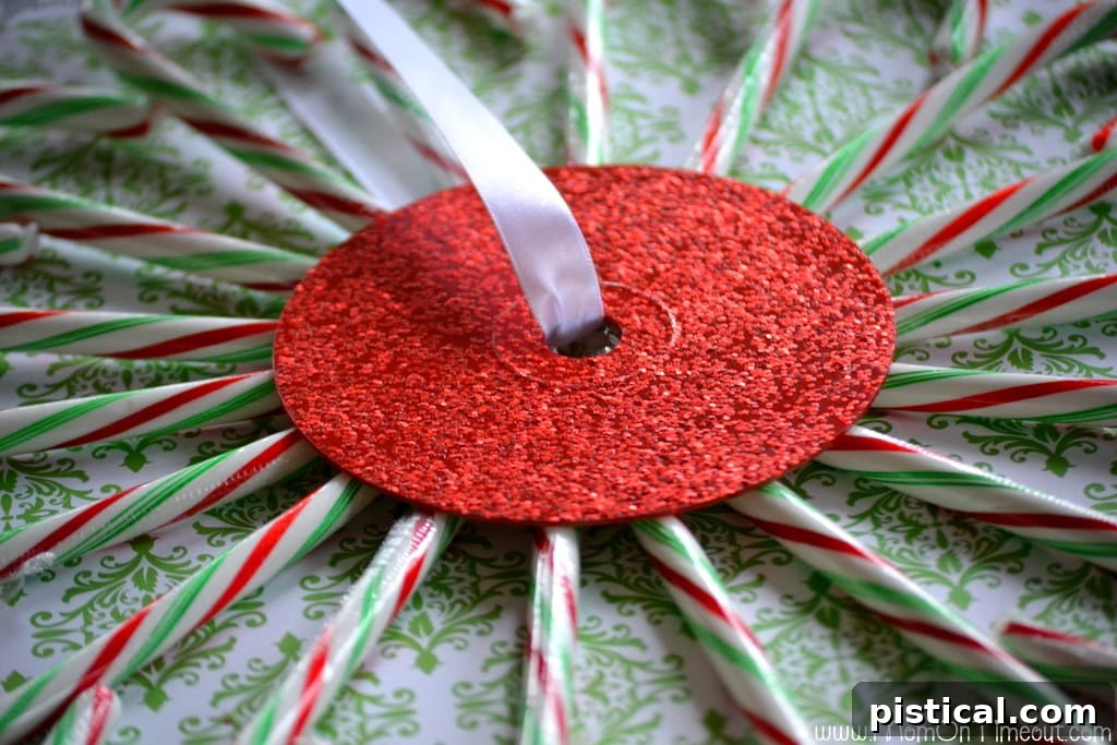 A festive ornament being hot glued to the center of the candy cane wreath, adding a finishing touch.