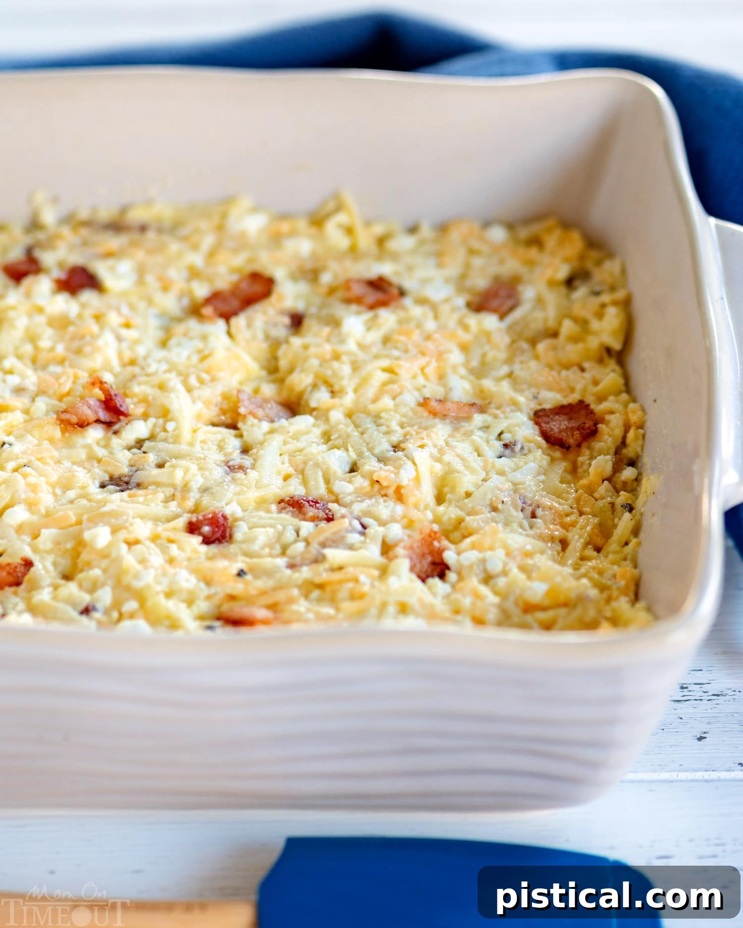 A close-up shot of a baked hash brown, bacon, and cheese breakfast casserole in a white dish, garnished with fresh chives.