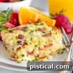 Serving of hash brown breakfast casserole on white round plate with fresh orange wedge and strawberries behind it.