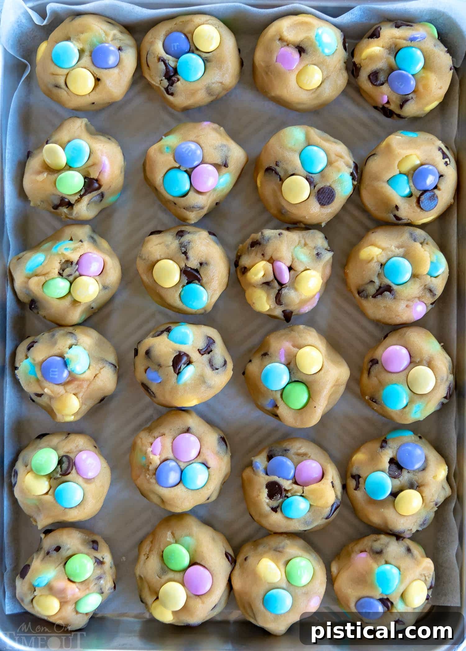 mm-chocolate-chip-cookies-baking-sheet-freezer - Frozen balls of M&M chocolate chip cookie dough on a parchment-lined baking sheet, ready for baking.