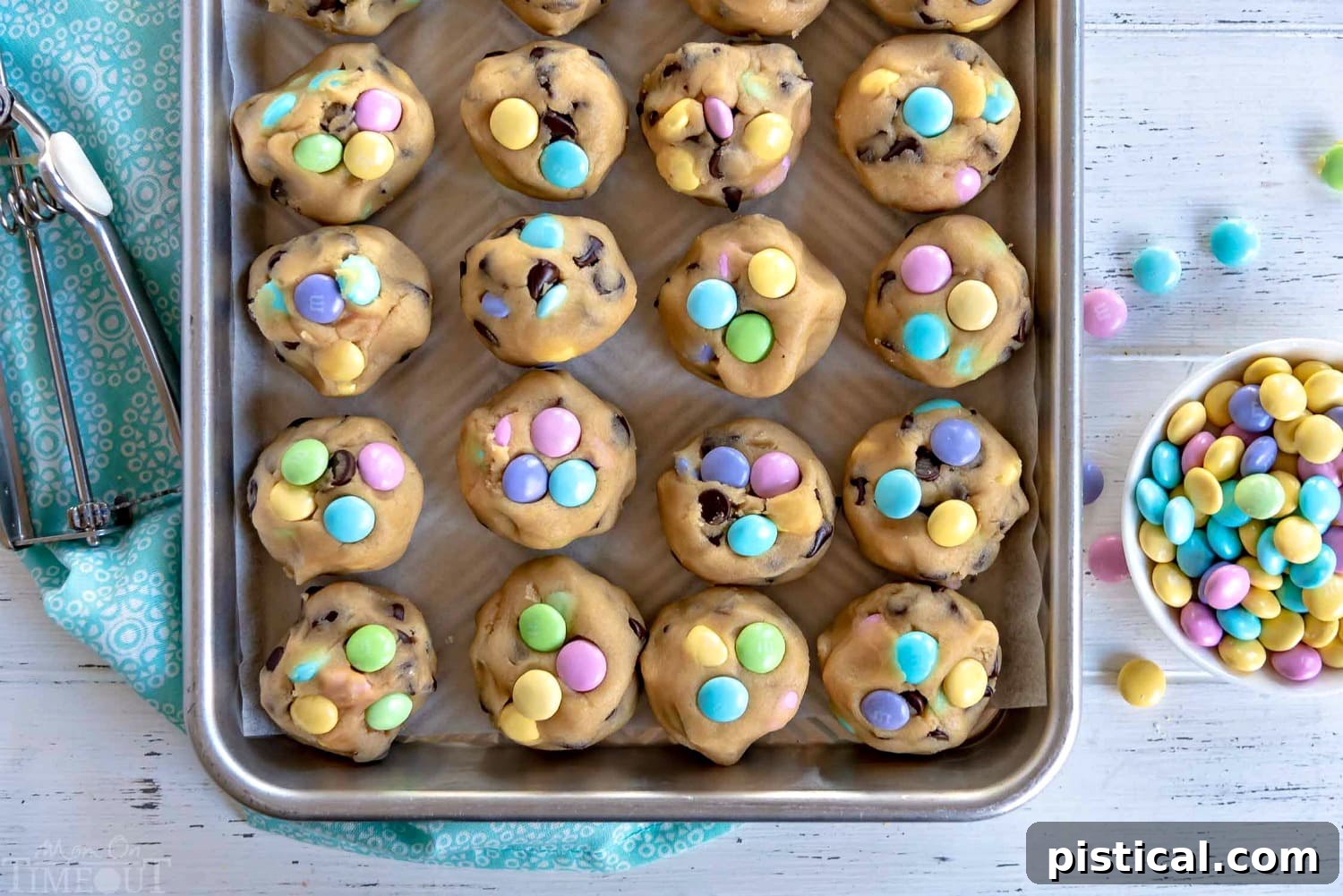 mm-chocolate-chip-cookie-dough-balls - Close-up of scooped, raw M&M chocolate chip cookie dough balls on a baking sheet, ready to be frozen.