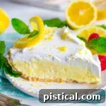 Lemon pie topped with whipped cream on a white plate with sliced lemons in the background, illustrating the perfect presentation.
