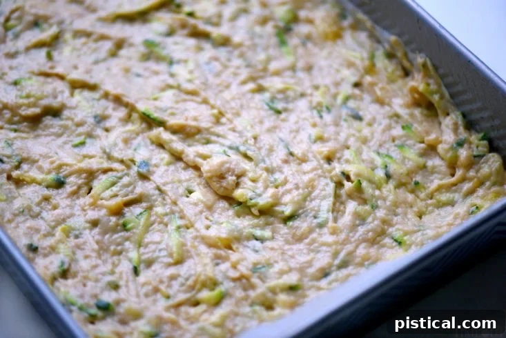 Zucchini Banana Cake batter being poured into a parchment-lined baking pan, showcasing its rich texture.