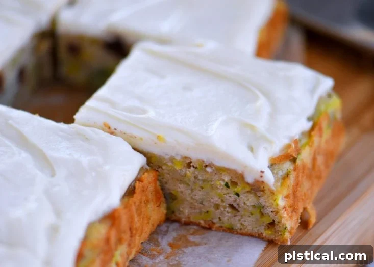 A single piece of moist Zucchini Banana Cake, topped with generous cream cheese frosting, on a white plate.