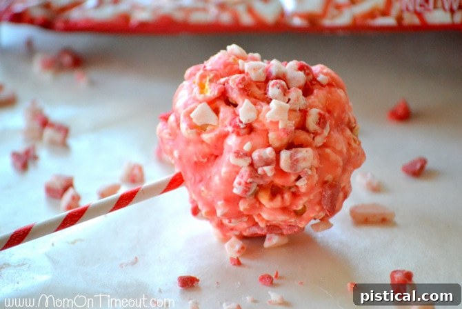 A freshly formed peppermint popcorn ball on a popsicle stick, being rolled in extra Andes Peppermint Crunch chips.