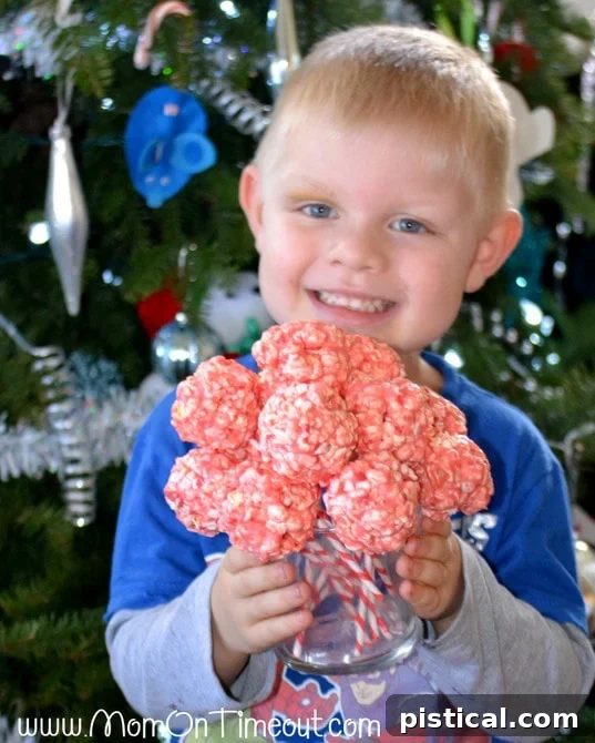 A young boy, Bryce, happily holding a peppermint crunch popcorn ball pop, excited to share his festive treats.