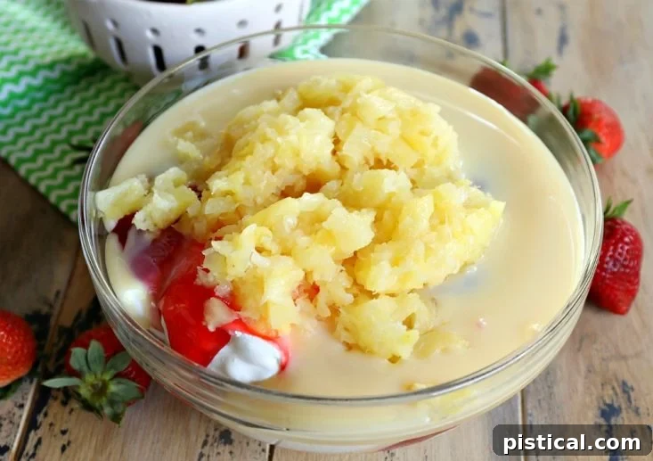 All the core ingredients for Strawberry Fluff, including Cool Whip, sweetened condensed milk, strawberry pie filling, crushed pineapple, marshmallows, and pecans, mixed together in a large glass bowl.
