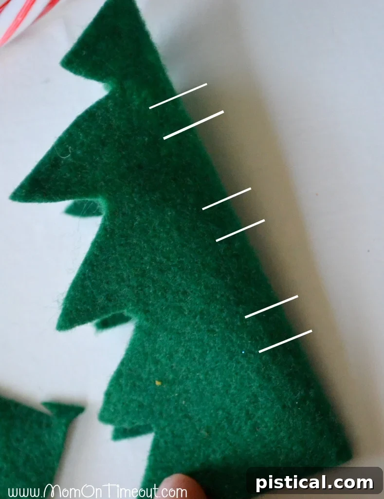 Close-up of a green felt Christmas tree with two horizontal slits cut near the base for candy cane insertion.