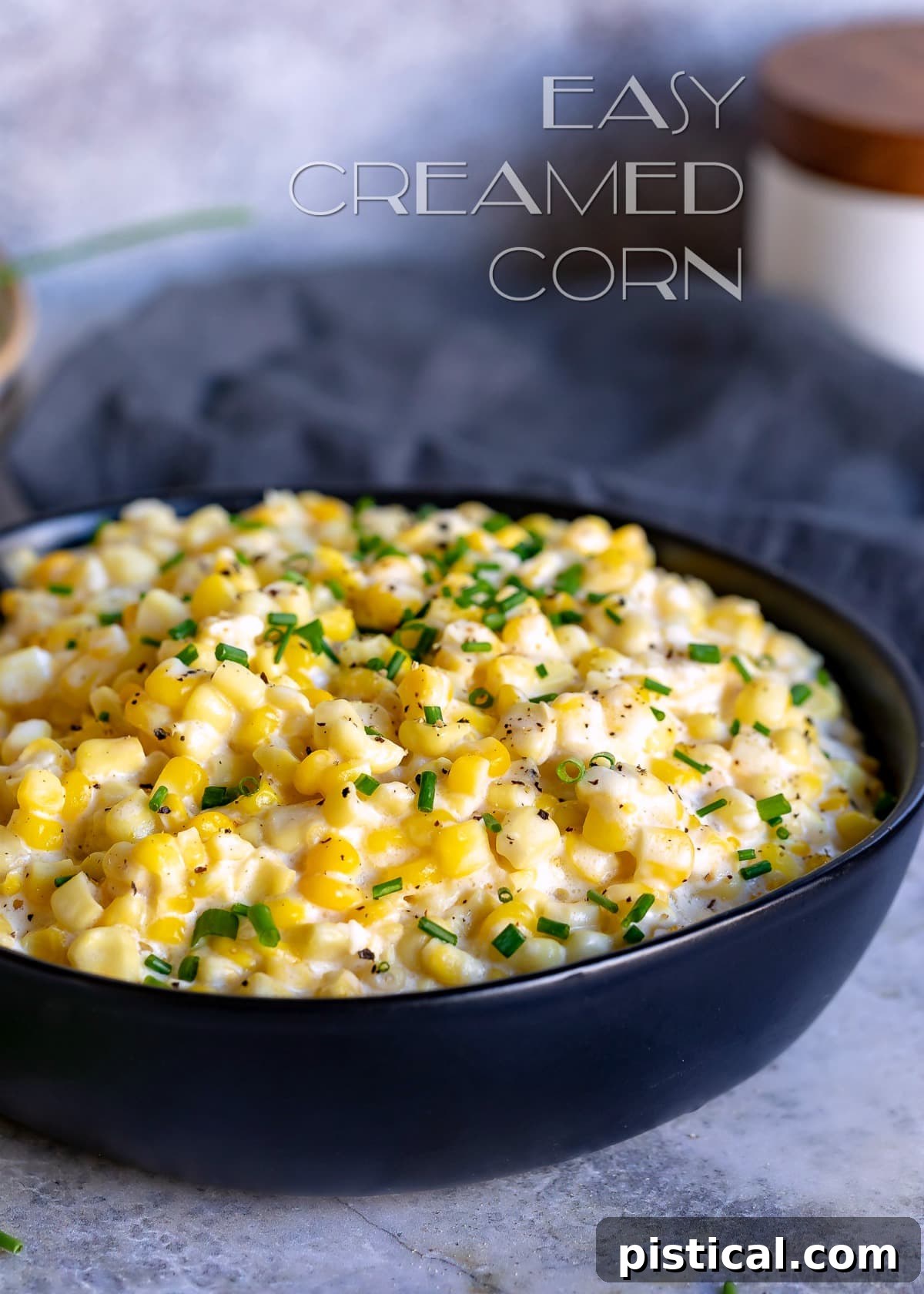 A black bowl brimming with creamy homemade creamed corn, garnished with fresh green chives, perfectly illustrating a decadent side dish.