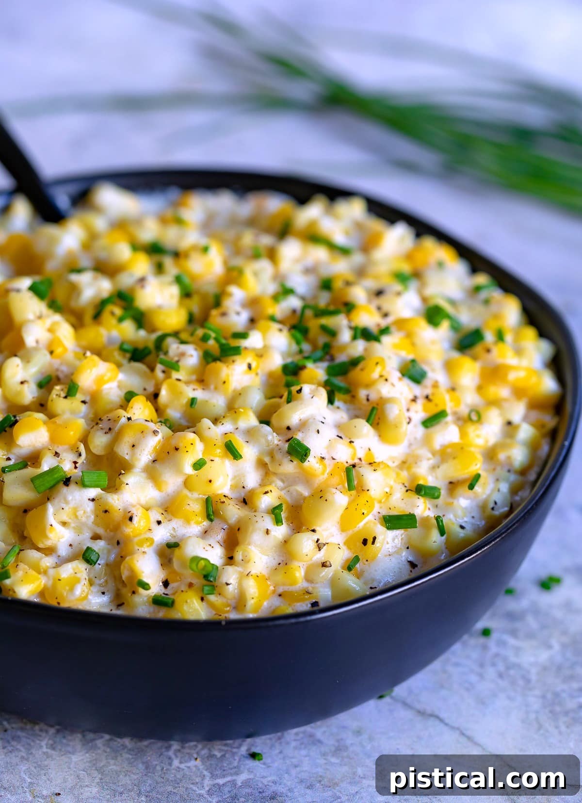 A top-down view of a serving bowl full of homemade creamed corn, featuring its creamy texture and fresh chive garnish, ready for family dinner.