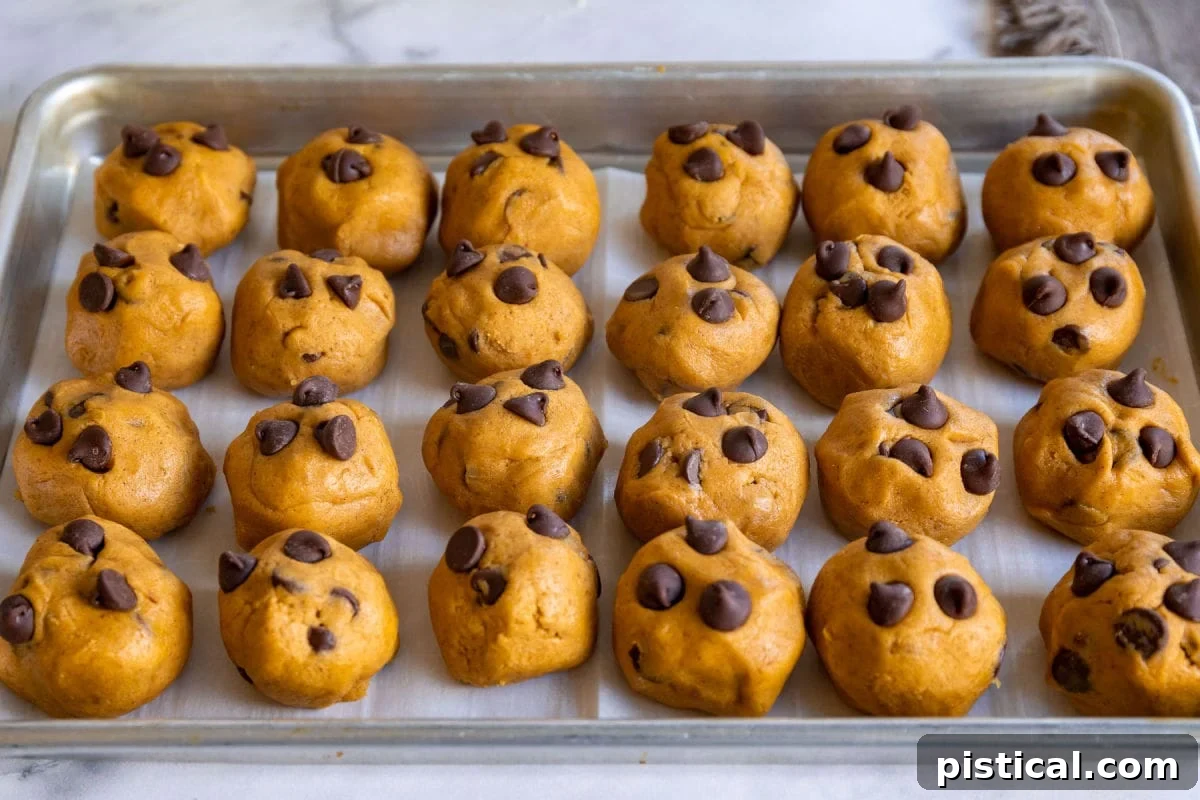 These Pumpkin Chocolate Chip Cookies are soft and chewy with loads of pumpkin flavor! Pumpkin pie spice and pumpkin puree work together to create an amazing pumpkin chocolate chip cookie recipe that's just perfect for the holidays! // Mom On Timeout #pumpkinchocolatechipcookies #pumpkin #chocolatechipcookies #cookies #baking #fall #holidays #thanksgiving #christmas Pumpkin chocolate chip cookies ready to be chilled, sitting on a parchment-lined quarter sheet pan.