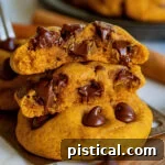 Two pumpkin chocolate chip cookies, one split in half and stacked, revealing melty chocolate chips.