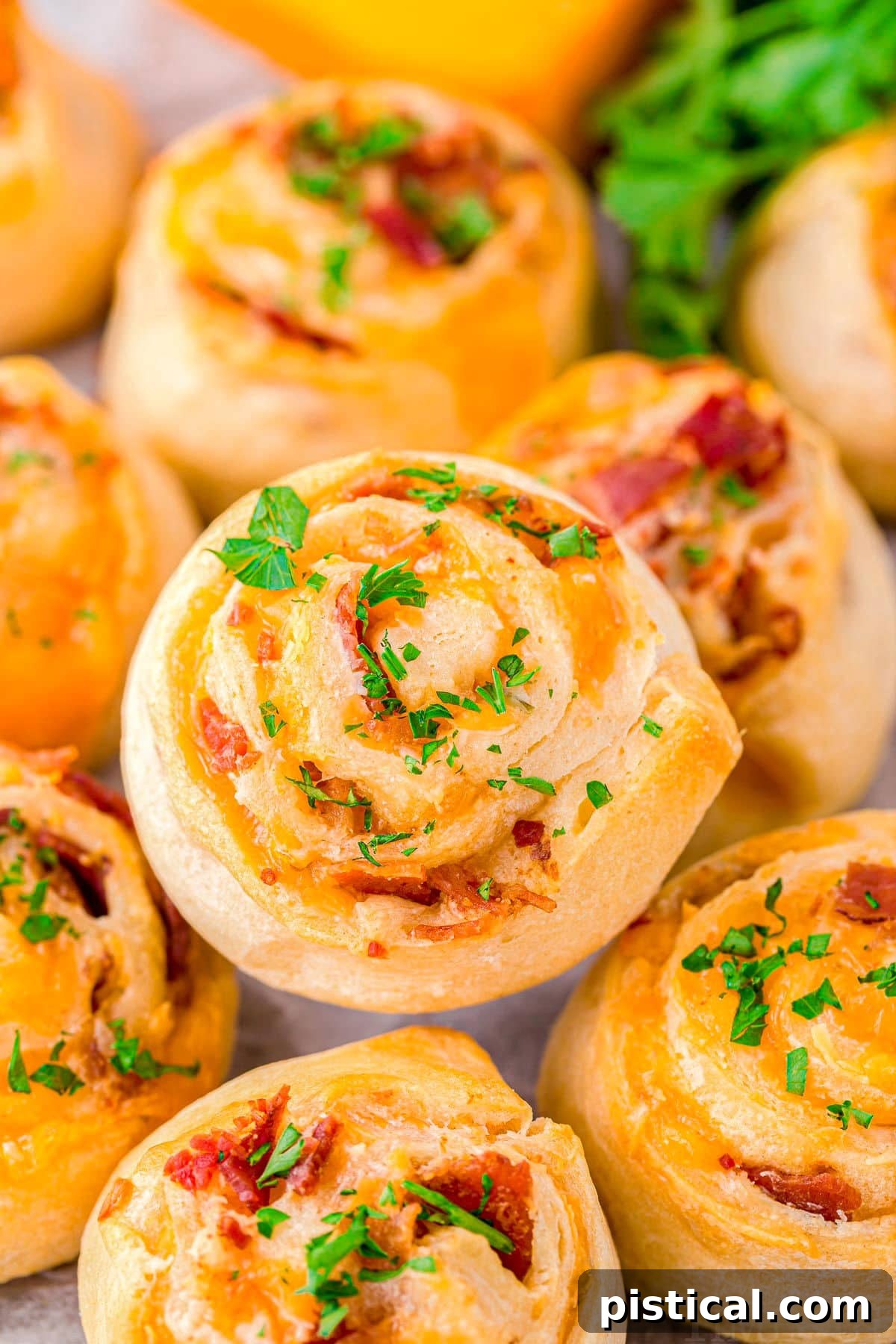Cheddar bacon pinwheels stacked on a plate, garnished with fresh chopped parsley, showcasing their golden-brown, flaky layers.