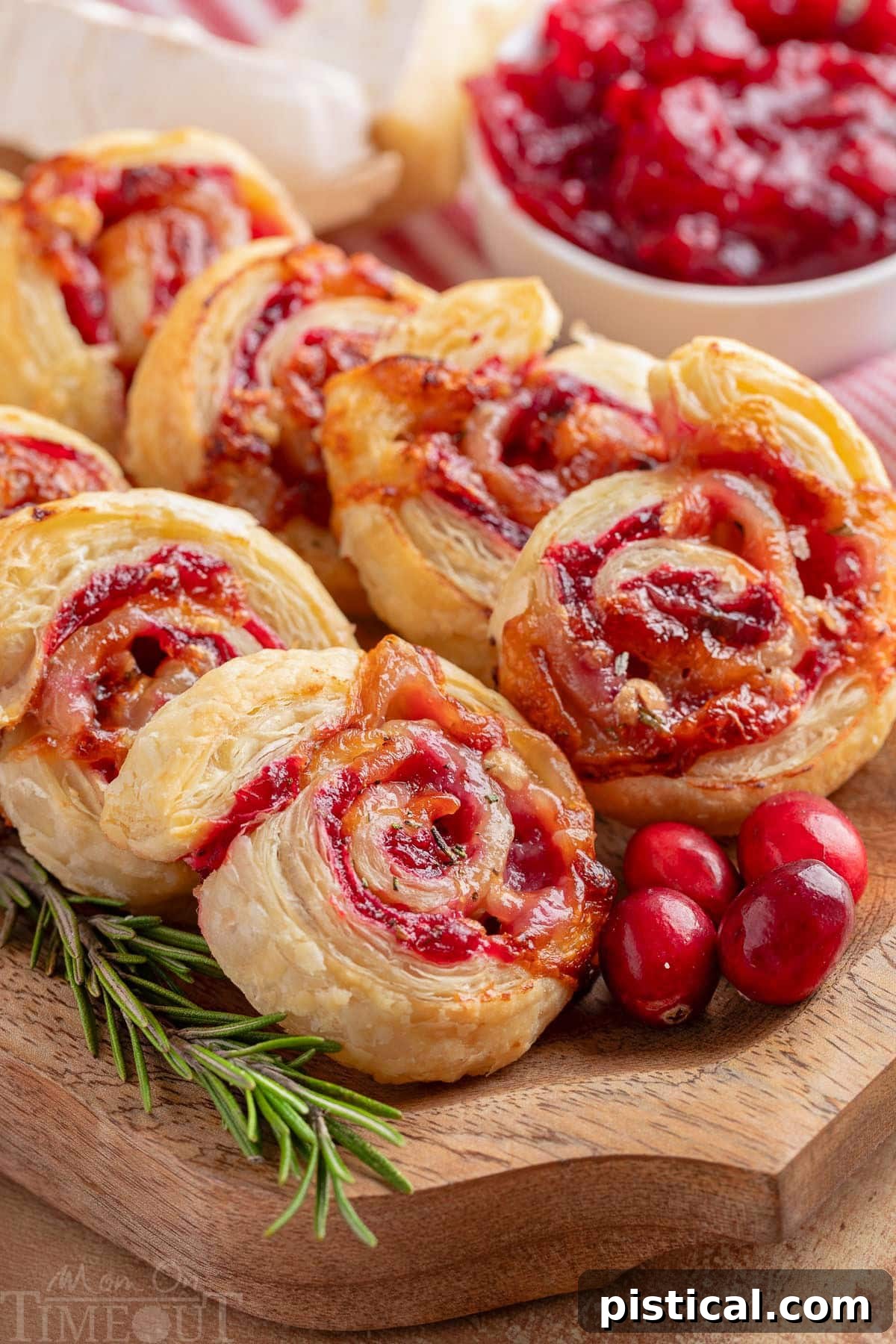 Elegant cranberry brie pinwheels arranged on a wood serving tray, garnished with fresh rosemary and bright cranberries for a festive touch.