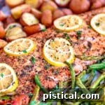 baked salmon with lemon slices on a sheet pan with green beans and red potatoes.