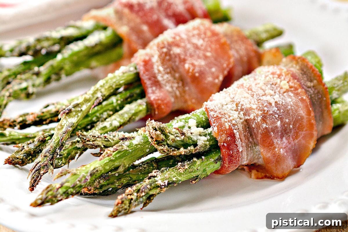 Close-up of three bacon wrapped asparagus bundles plated on a white dish, ready to eat.