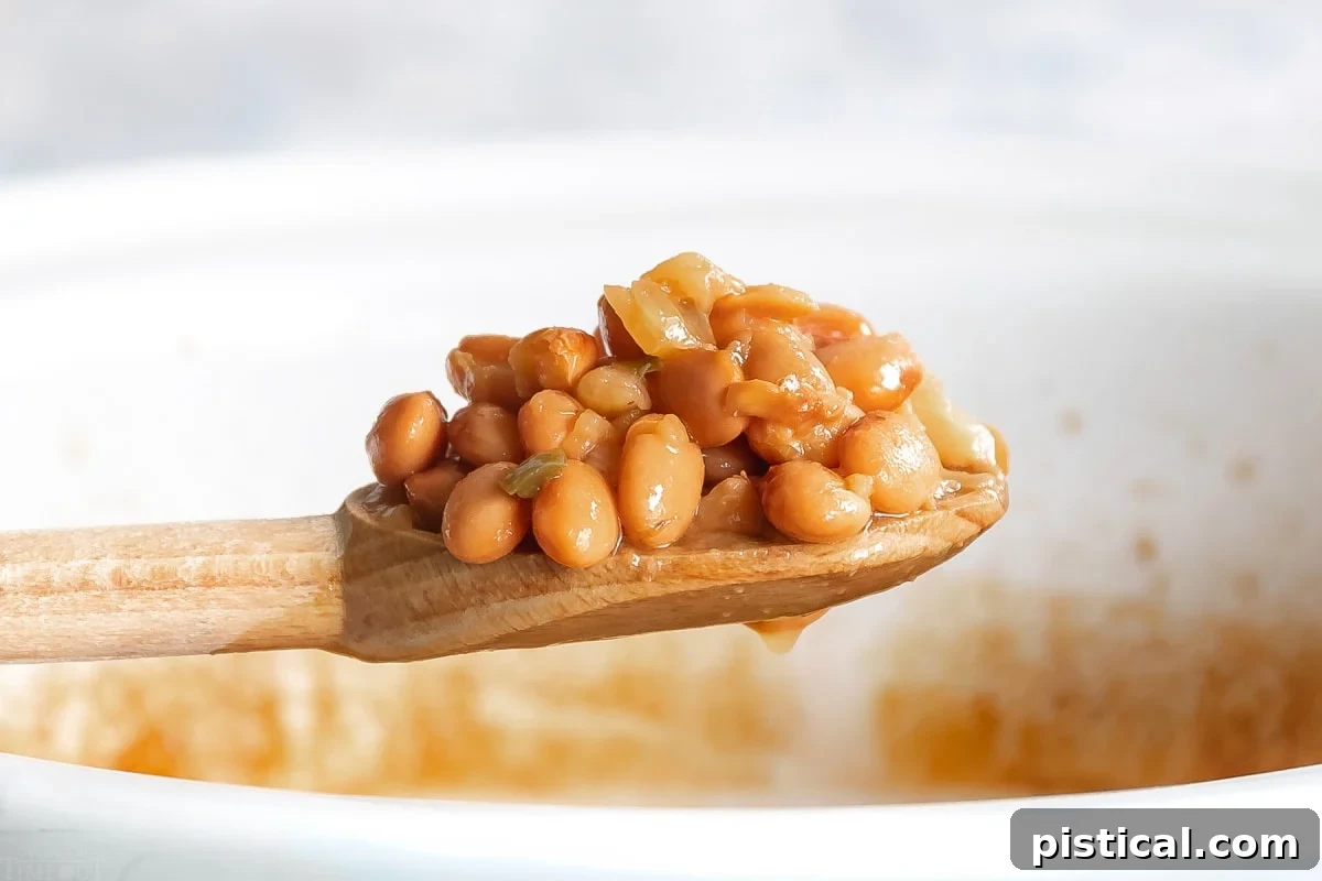 Crock pot pinto beans on a wooden spoon held over a white crockpot, wide shot