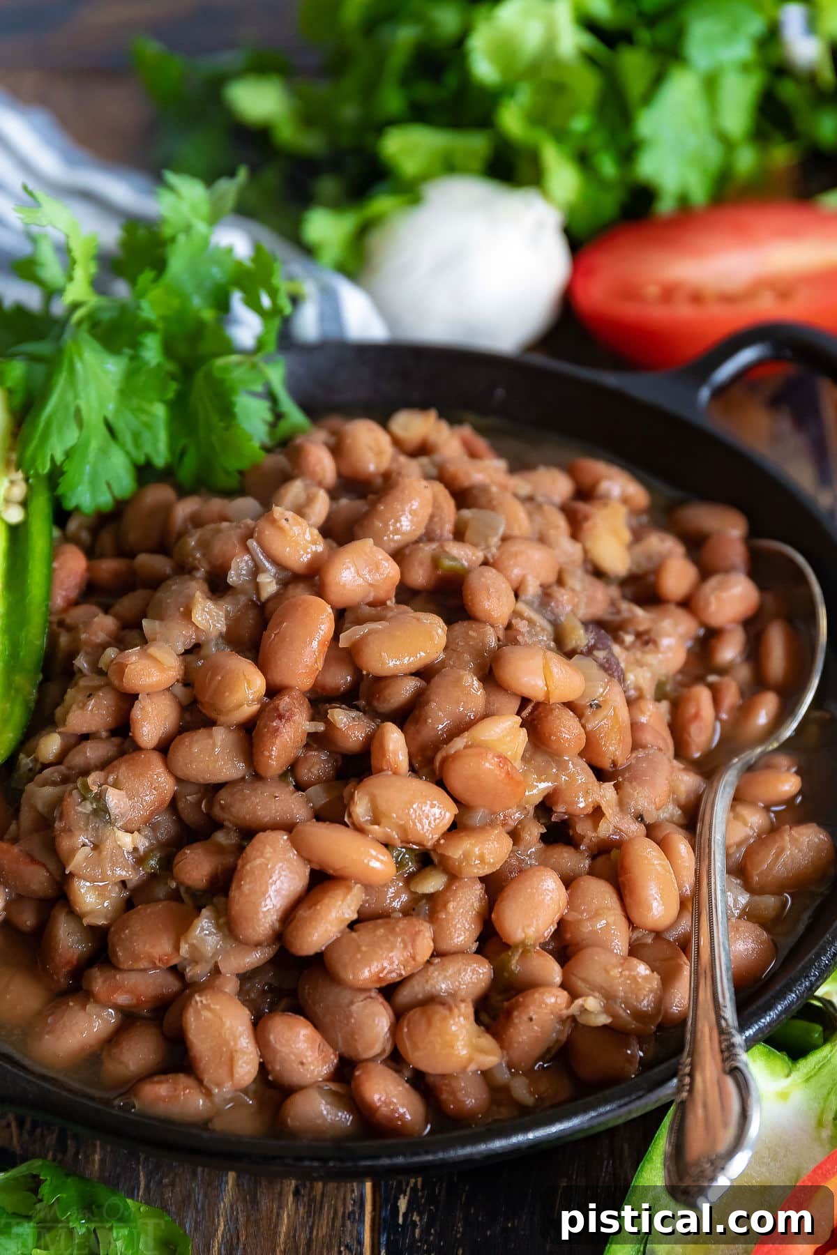 Slow cooker pinto beans in a black bowl with a spoon, garnished with jalapeno and cilantro