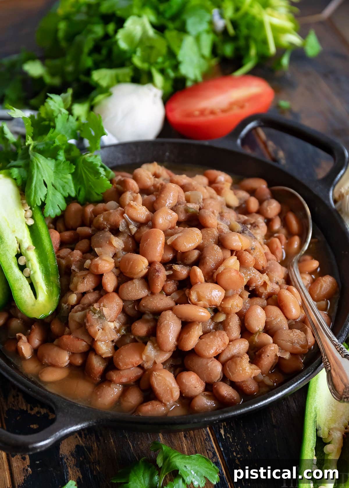 Slow cooker pinto beans in a black bowl with a spoon, garnished with jalapeno, tomato, and cilantro