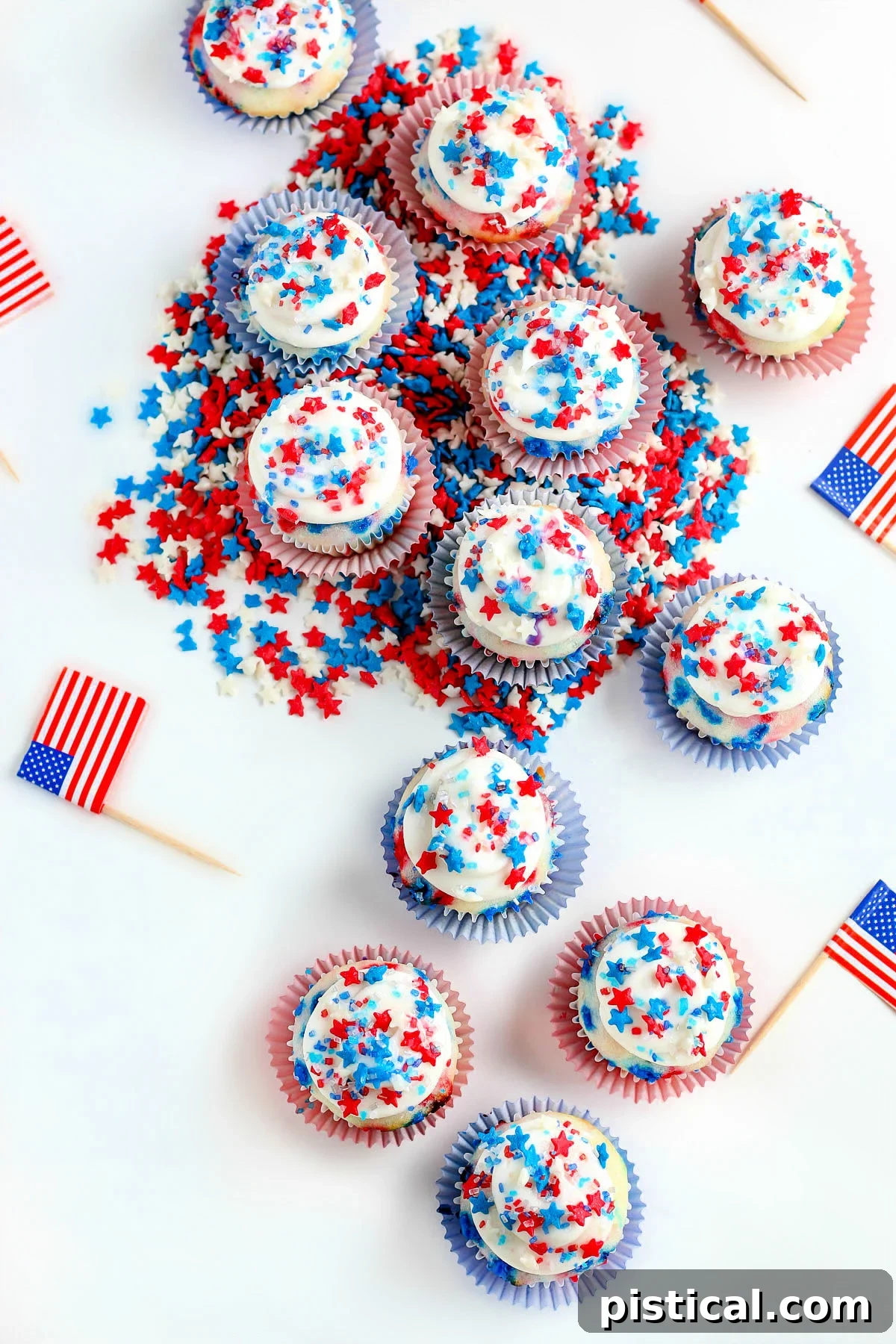 Top-down view of dozens of freshly baked mini vanilla cupcakes, generously adorned with festive red, white, and blue star sprinkles.