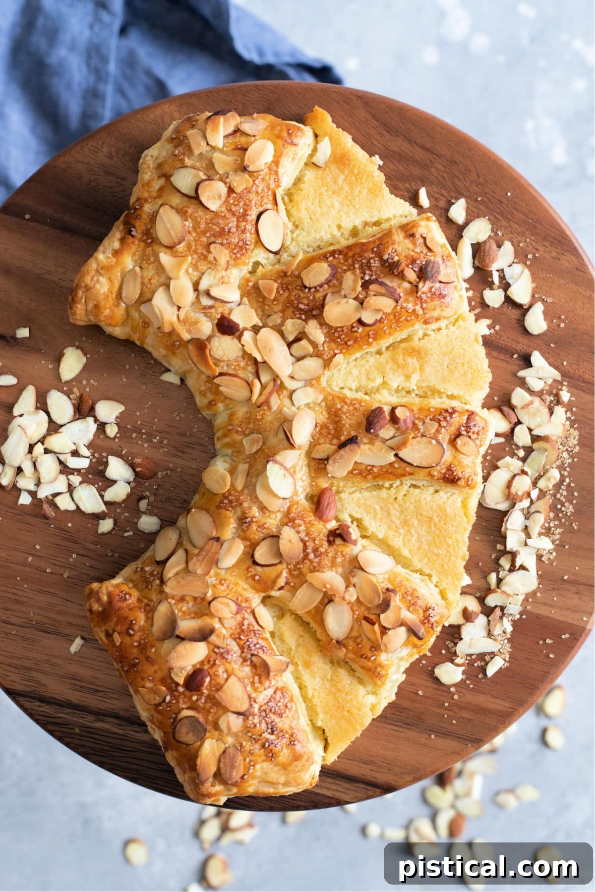 Top-down view of a golden brown almond bear claw pastry on an elegant cake pedestal with a soft blue napkin underneath.