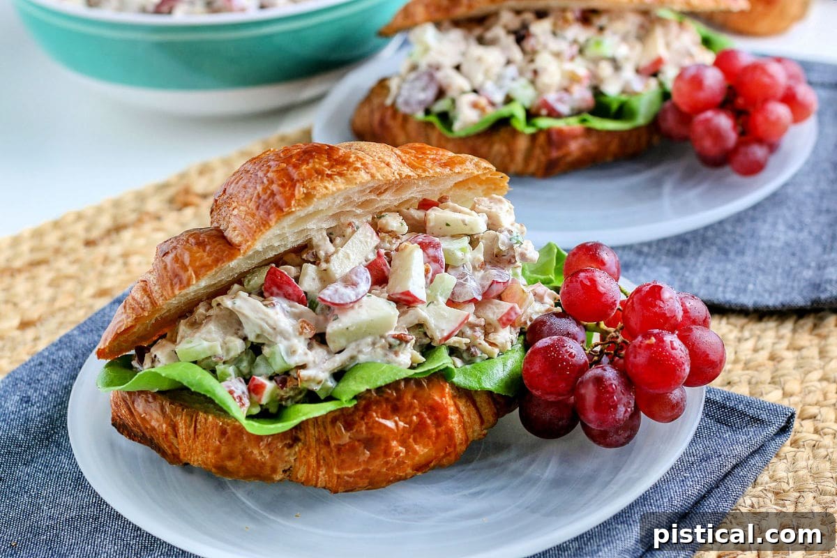 chicken salad on croissant sitting on glass plate with grapes on the side blue napkin underneath
