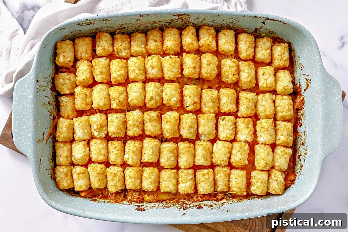 A freshly baked Taco Tater Tot Casserole sits in a rectangular baking dish on a wooden cutting board, ready to be served. The tater tots on top are golden and crispy, with melted cheese peeking through.