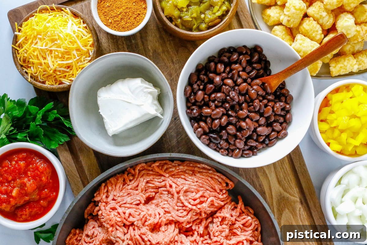 Individual ingredients for Taco Tater Tot Casserole are neatly arranged in bowls on a wooden surface, including ground beef, diced onions and bell peppers, salsa, black beans, various shredded cheeses, and a bag of tater tots.