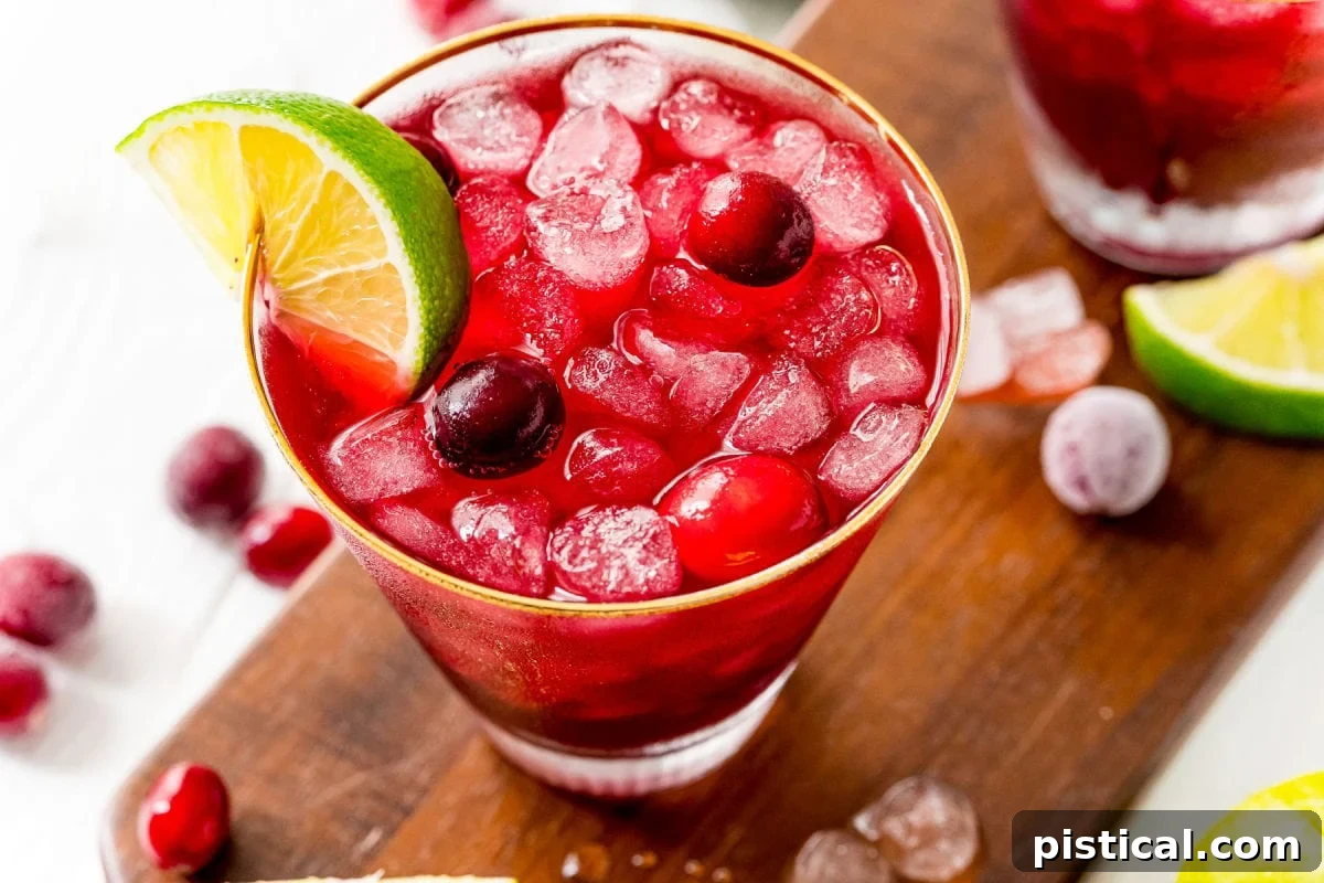vodka cranberry cocktail in glass with lime wedge and cranberries sitting on dark wood board