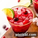 vodka cranberry cocktail in glass with lime wedge and cranberries sitting on dark wood board