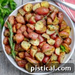 white plate with roasted potatoes garnished with fresh herbs and red towel underneath