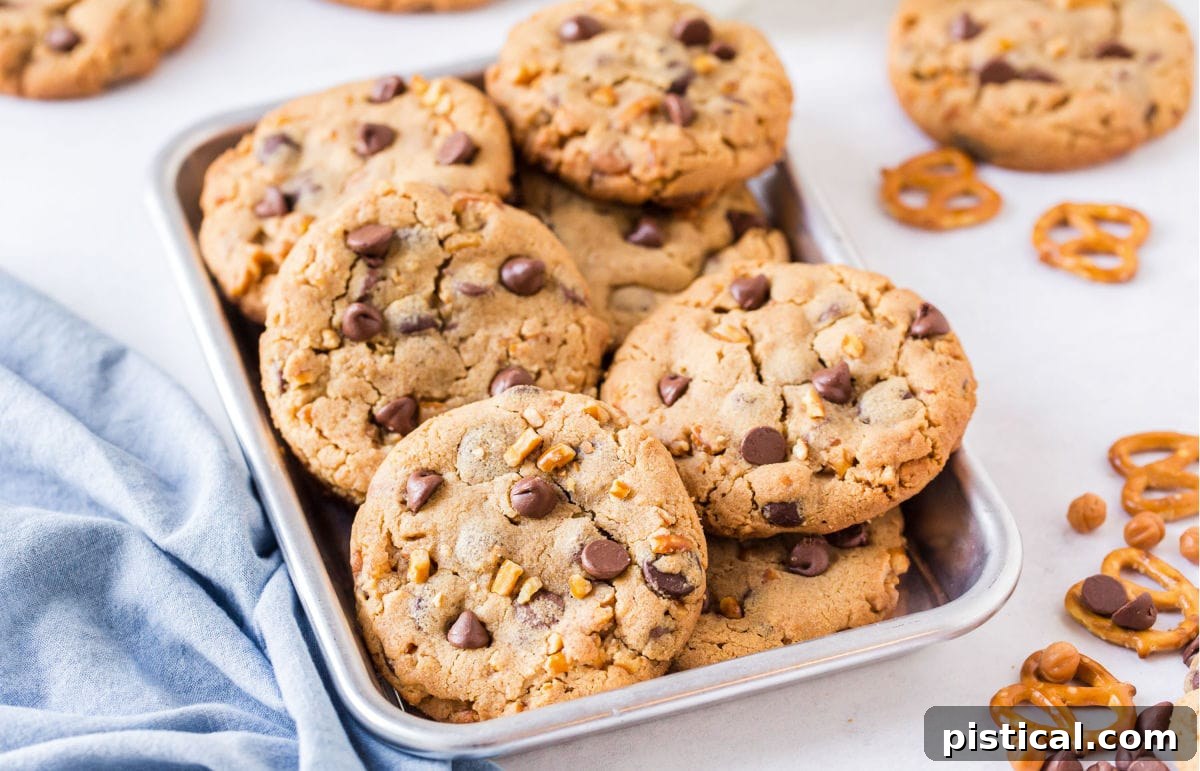 Many Loaded Peanut Butter Chocolate Chip Cookies artfully piled in a small metal sheet pan with a blue napkin beside them.