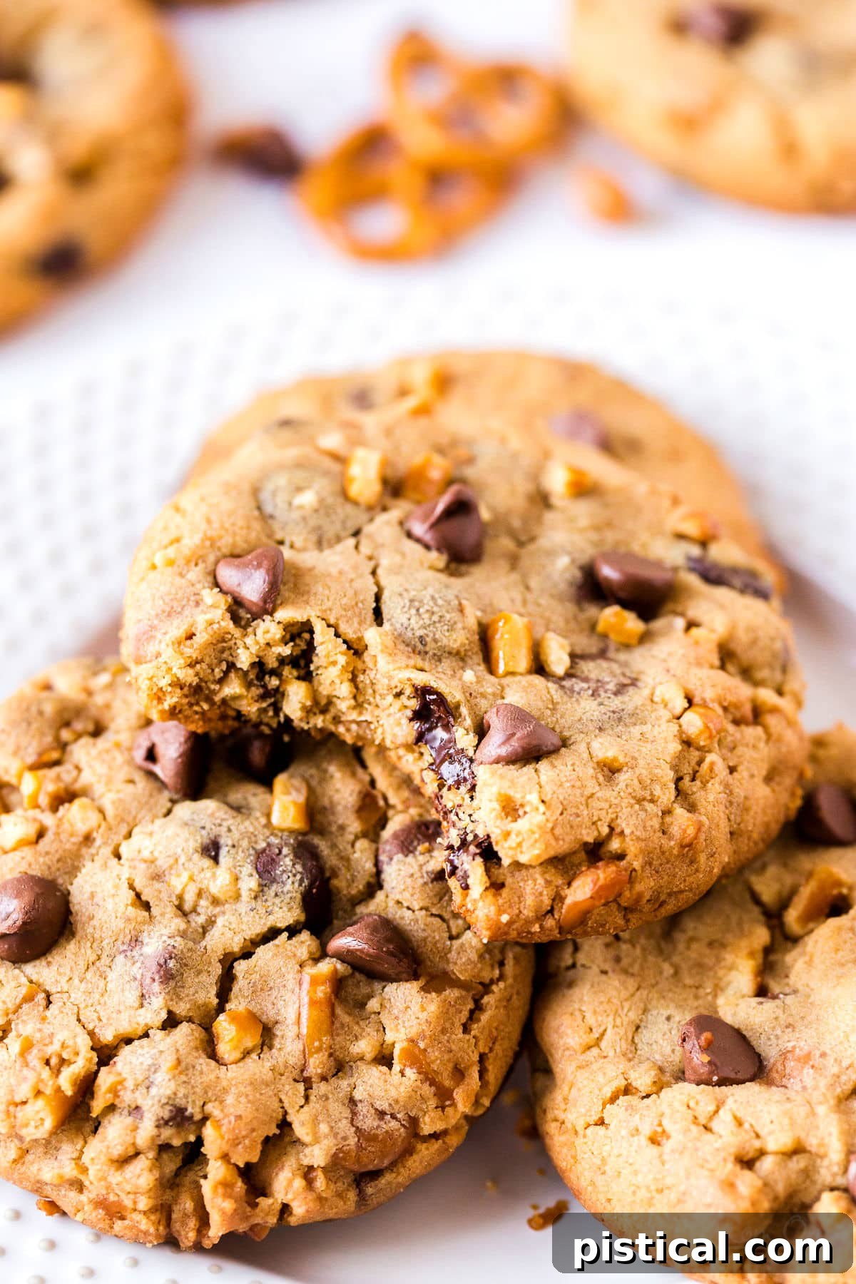 Three Loaded Pretzel Chocolate Chip Cookies arranged on a white plate, with a bite taken out of the top cookie.