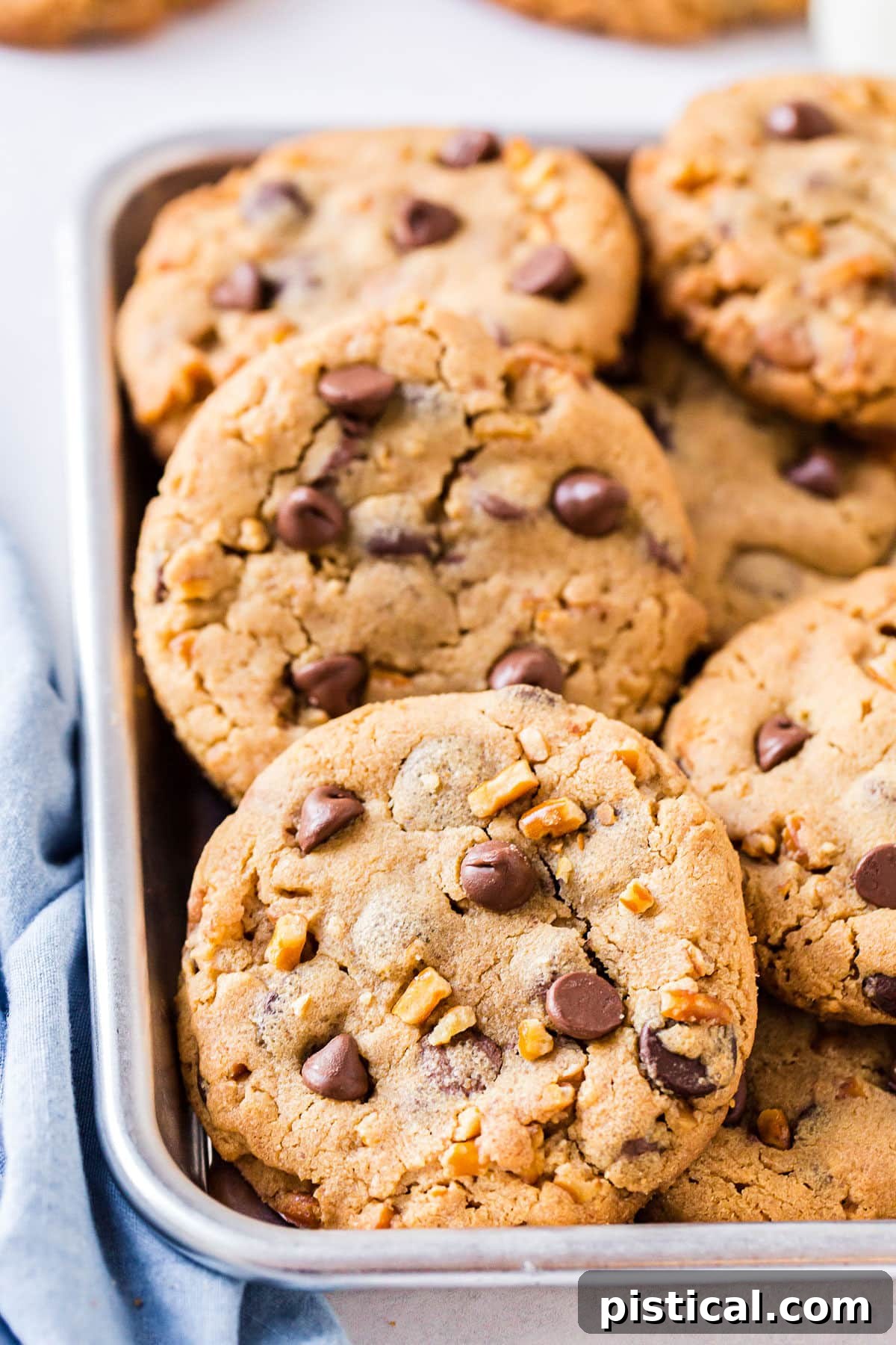 Chocolate chip cookies piled high in a small silver tray, with a blue napkin casually placed on the side.