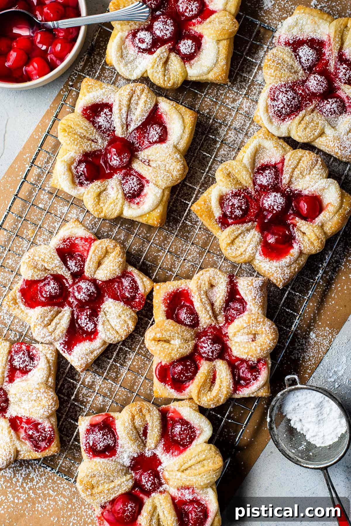 Top-down view of freshly baked cherry cheese danishes on brown parchment paper, lightly dusted with powdered sugar.