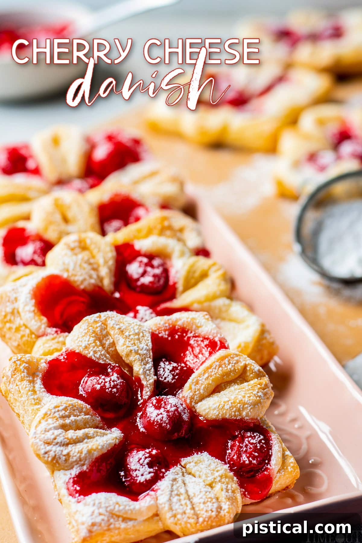Cherry cheese danishes artfully arranged on a light pink tray, generously dusted with powdered sugar.