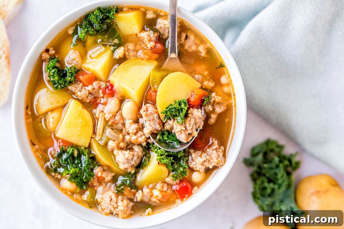 A top-down view of a white bowl filled with Sausage Kale Soup, garnished with fresh herbs and a light mint napkin resting elegantly to the side.